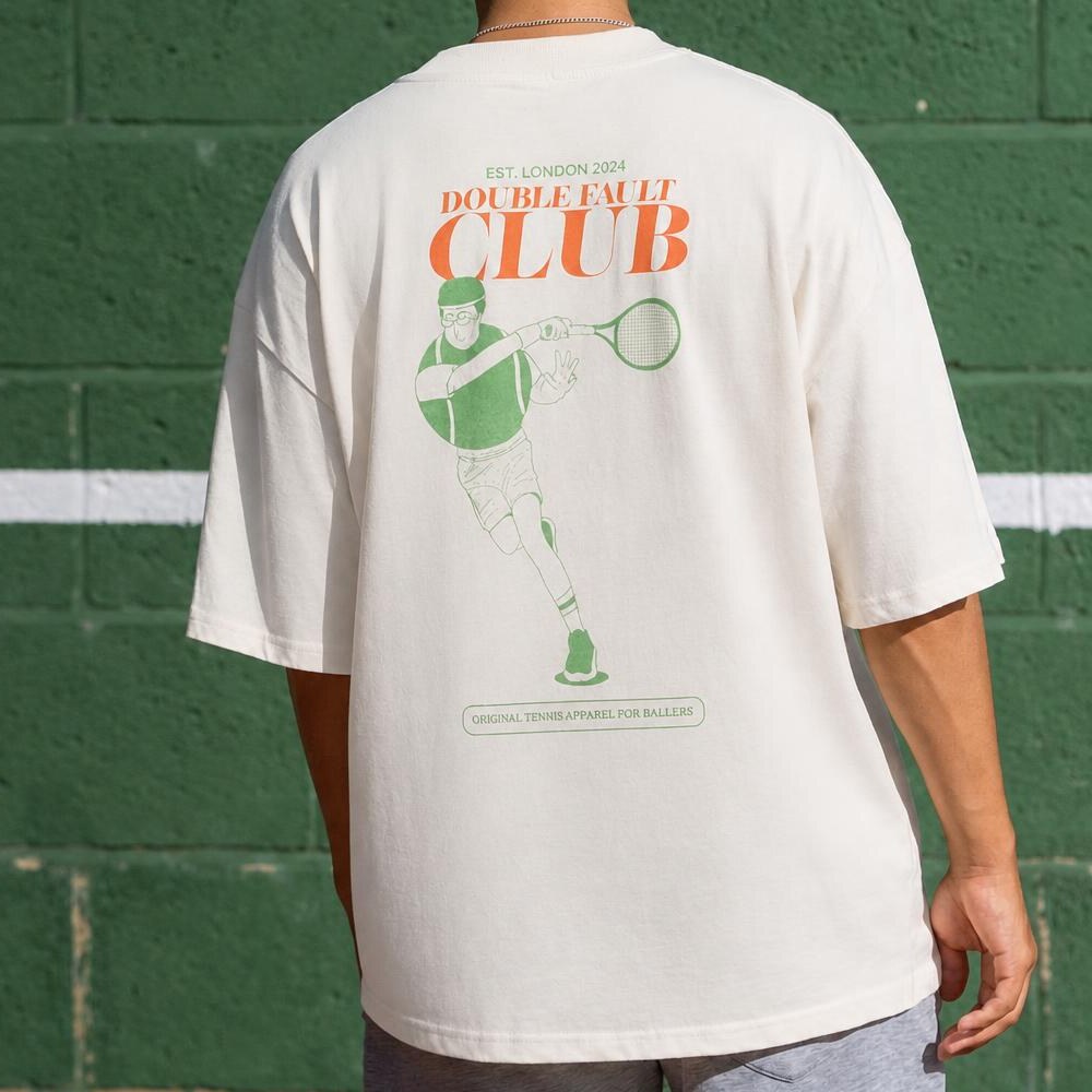 Double Fault Club back print on a naturally draped tee, worn against a green tennis-court wall