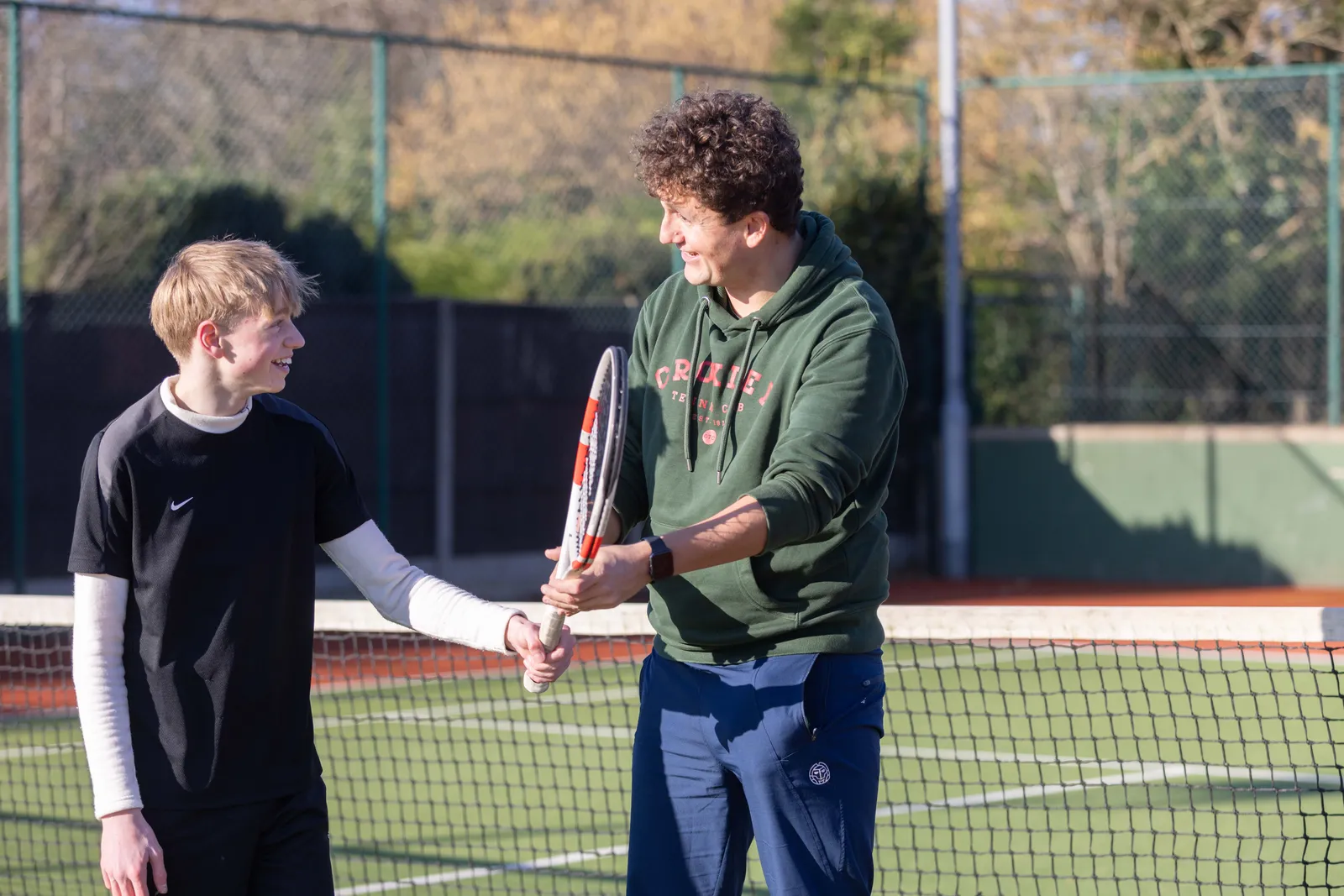 A friendly Tennis by Sam coach encouraging a child on court